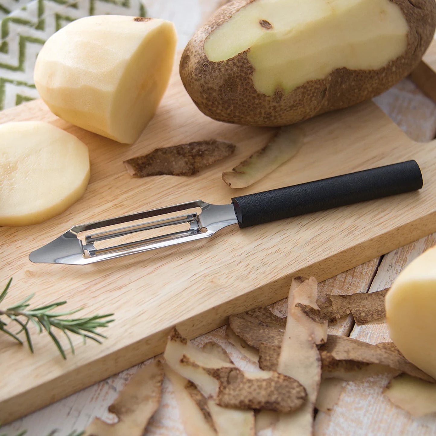 Handcrafted vegetable peeler with razor-sharp stainless steel blade and durable black resin handle resting on a wooden board surrounded by peeled potatoes and skins, ideal for Kitchen & Food, Specialty Equipment, Peelers and Pitters, USA Made, Best Sellers, Promo Eligible collections.