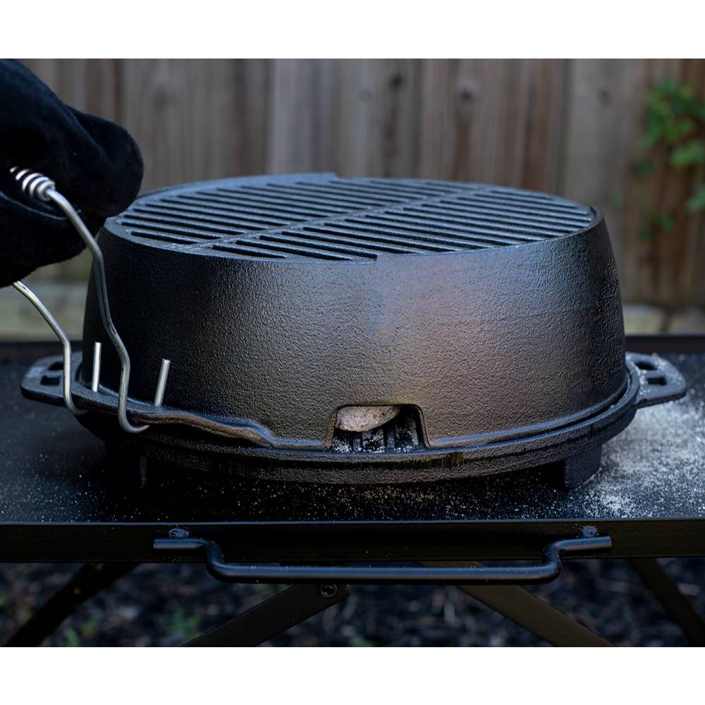 Handcrafted portable cast iron grill with detachable spring handles, heated over charcoal on a sturdy outdoor table, perfect for camping, grilling, and outdoor cooking.