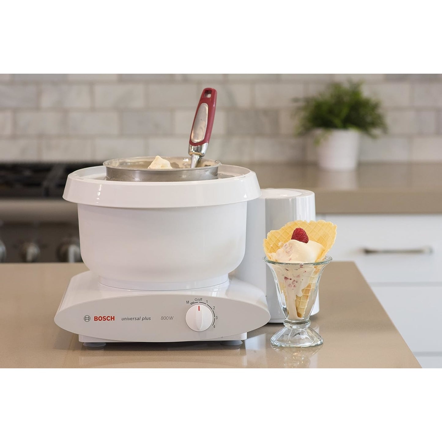 White ice cream maker attachment with stainless steel bowl and red-handled paddle on a countertop, next to a glass of ice cream with wafer, featured in Kitchen Gadgets and Best Sellers collections.