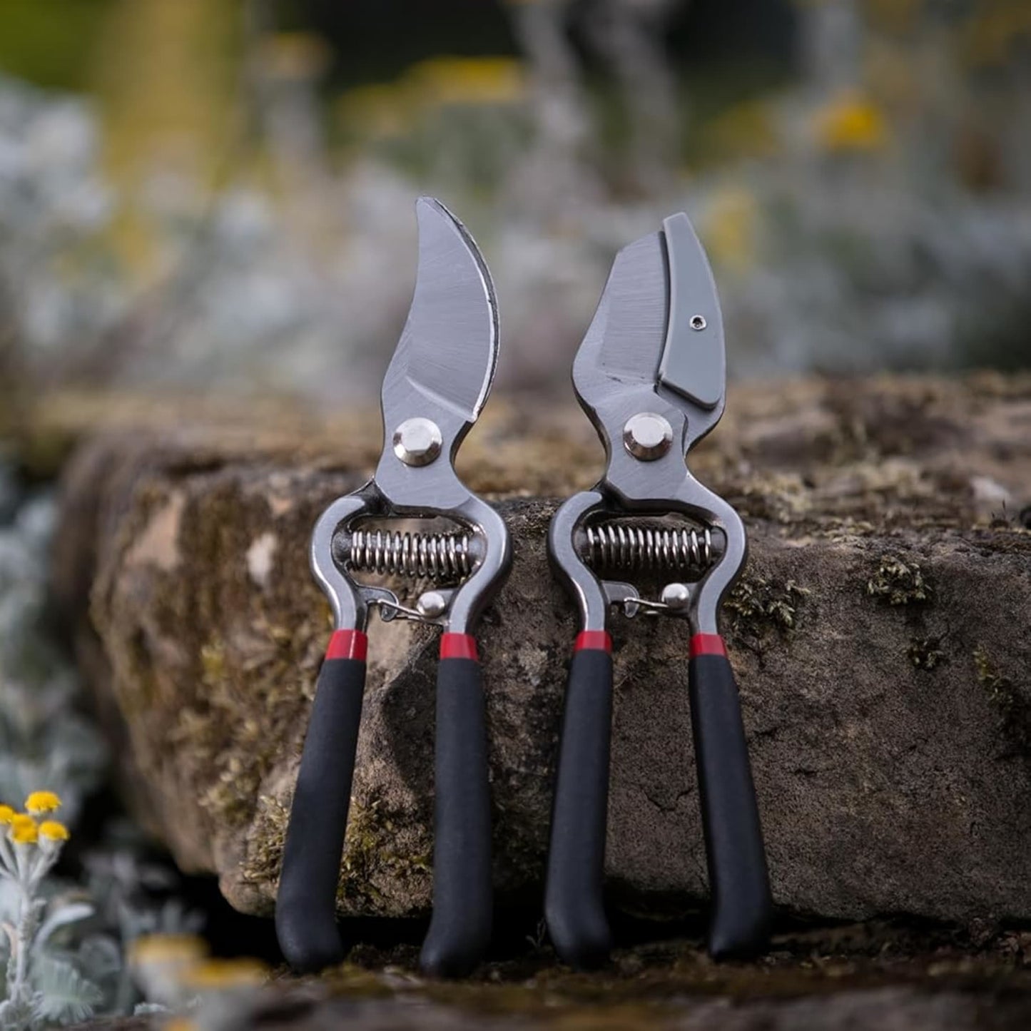 Pair of drop-forged bypass and anvil pruners with black handles and red accents resting on a tree stump in a garden setting, suited for Farm, Garden & Tool and Lawncare collections.