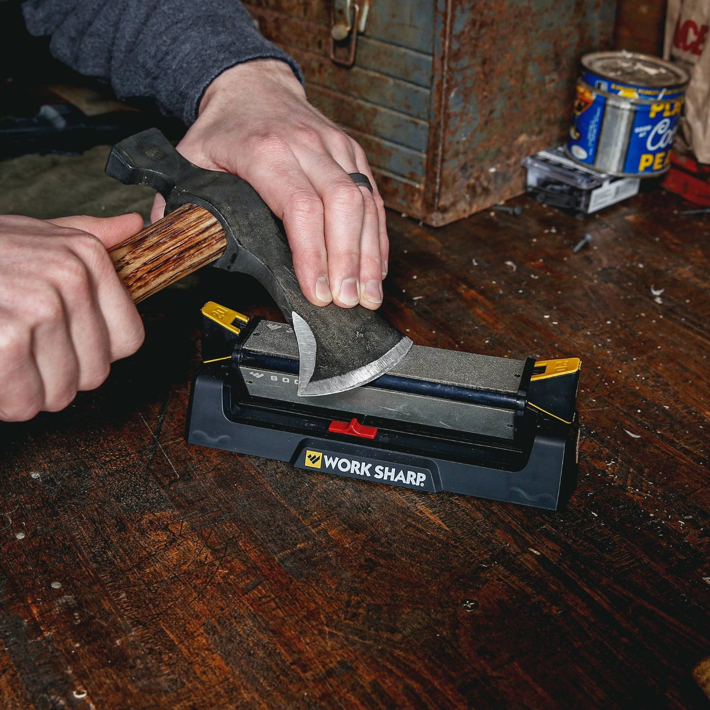Person sharpening an axe with a wooden handle on a Work Sharp benchstone sharpener featuring coarse and fine abrasive surfaces, on a rustic wooden workbench, ideal for Farm, Garden & Tool, Hand Tools and Hardware, and Sharpening collections.