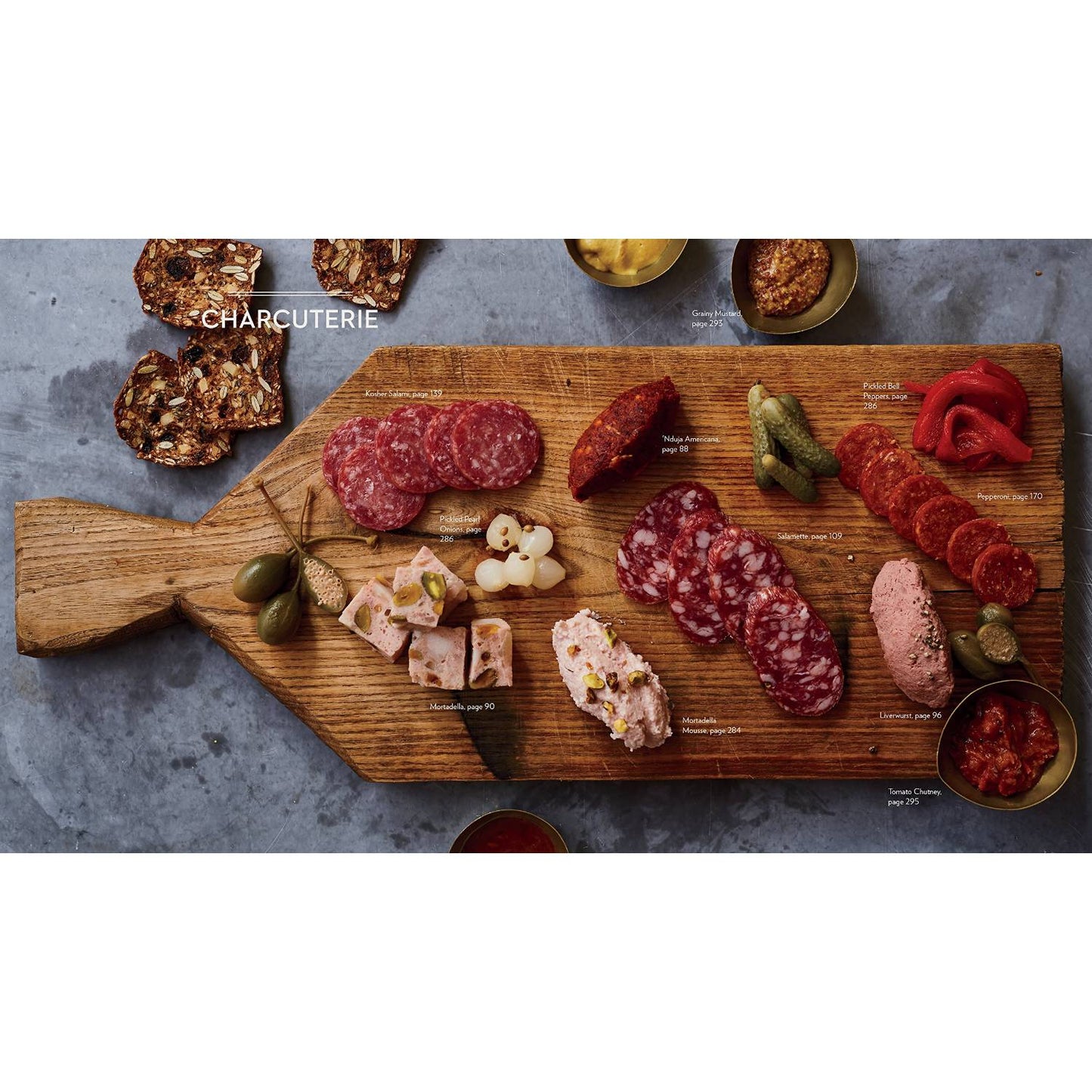 Wooden cutting board with an assortment of sliced cured meats, pâté, pickles, and crackers arranged in a handcrafted rustic style, suitable for cookbooks, best sellers, and home and garden how-to collections.
