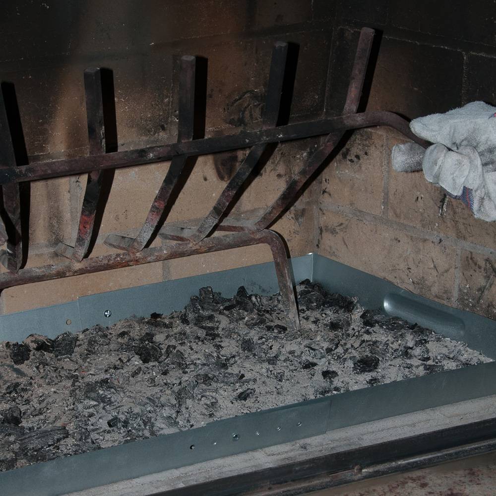 Galvanized steel fireplace tray under a metal grate filled with cooled ashes and hot coals being adjusted, suited for Hearth Accessories, Stoves, Best Sellers, and Promo Eligible collections.