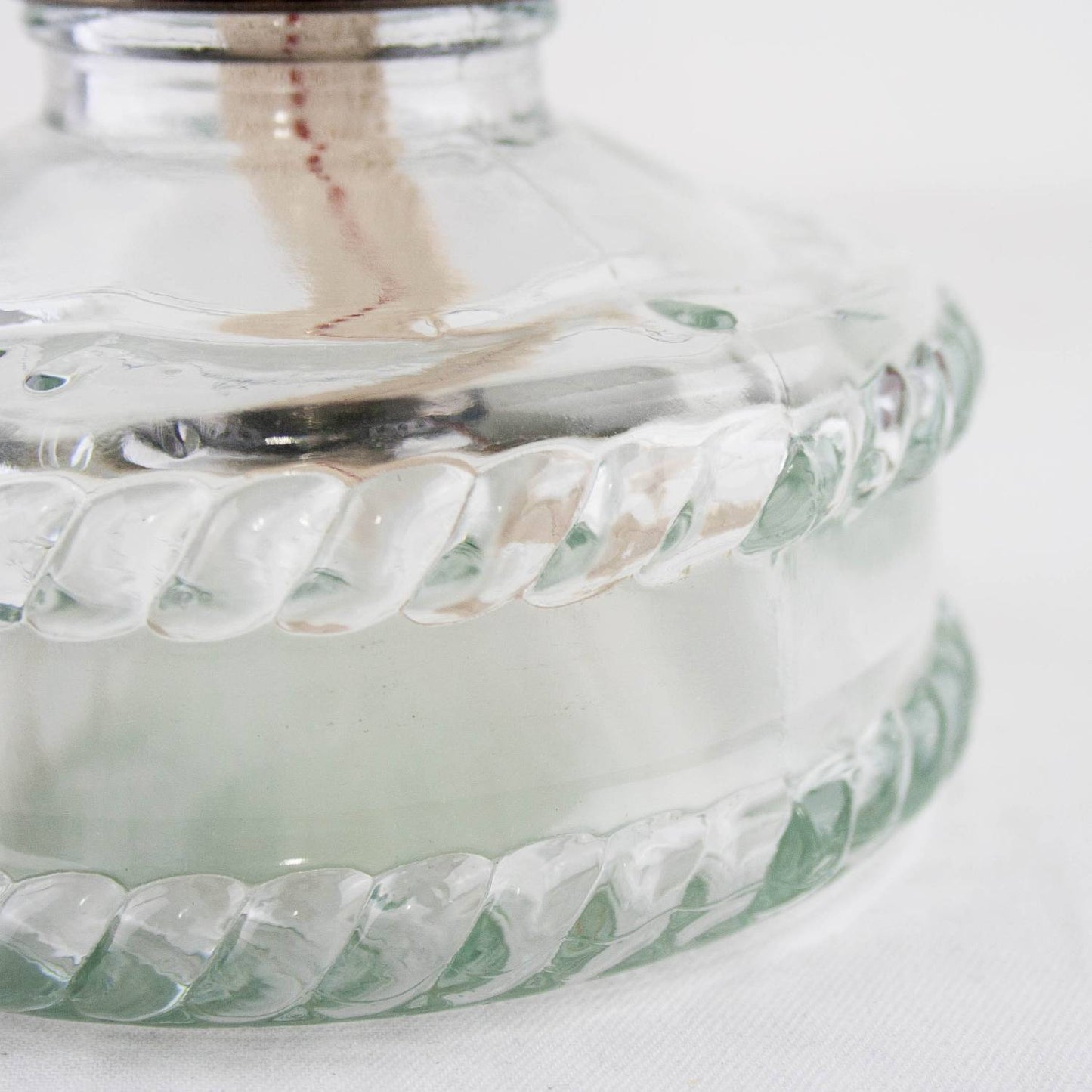 Close-up of a clear glass fuel base with a twisted pattern, showing the fabric wick inside, handcrafted oil lamp suitable for Lamps & Lighting, Oil Lamps, Wall Lamps, and Best Sellers collections.