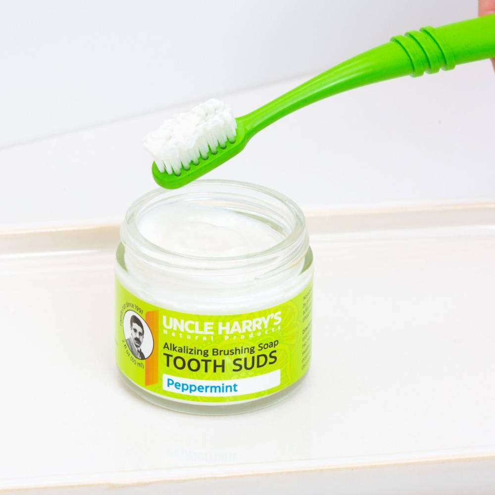 Open jar of Uncle Harry's handcrafted peppermint brushing soap tooth suds with a bright green toothbrush holding foamy suds, part of USA made Health & Wellness grooming collection.