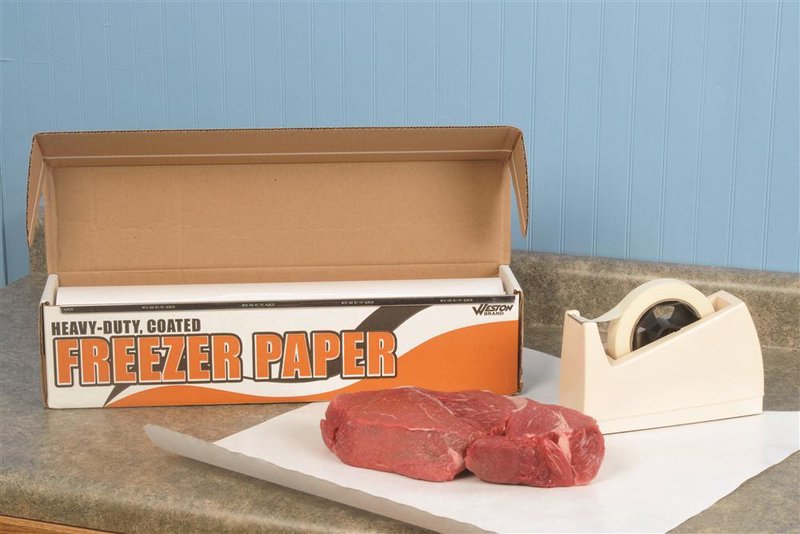 Box of heavy-duty coated freezer paper roll with white dispenser on countertop next to two raw beef steaks on a sheet of paper, suited for Kitchen & Food and Butchering Supplies collections.