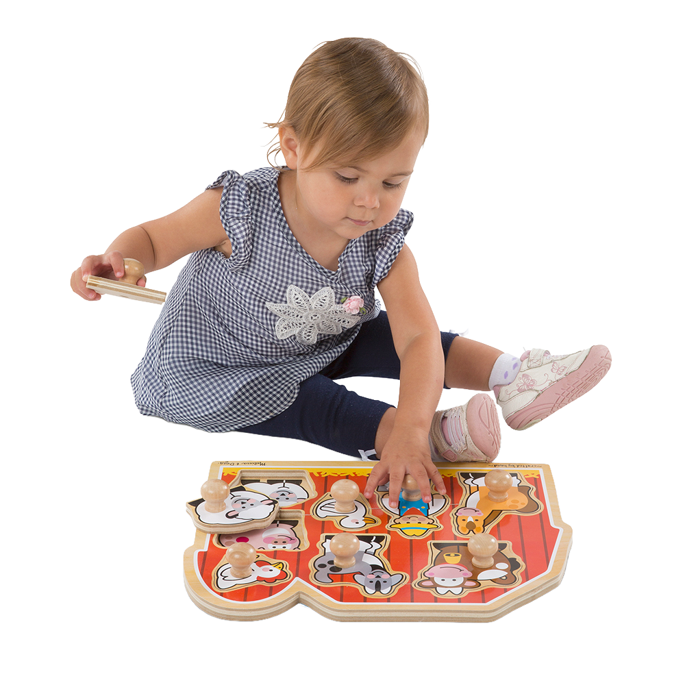 Toddler sitting and playing with a handcrafted wooden farm animal puzzle featuring jumbo knobs on a bright red barn background, encouraging fine motor skills development in children.