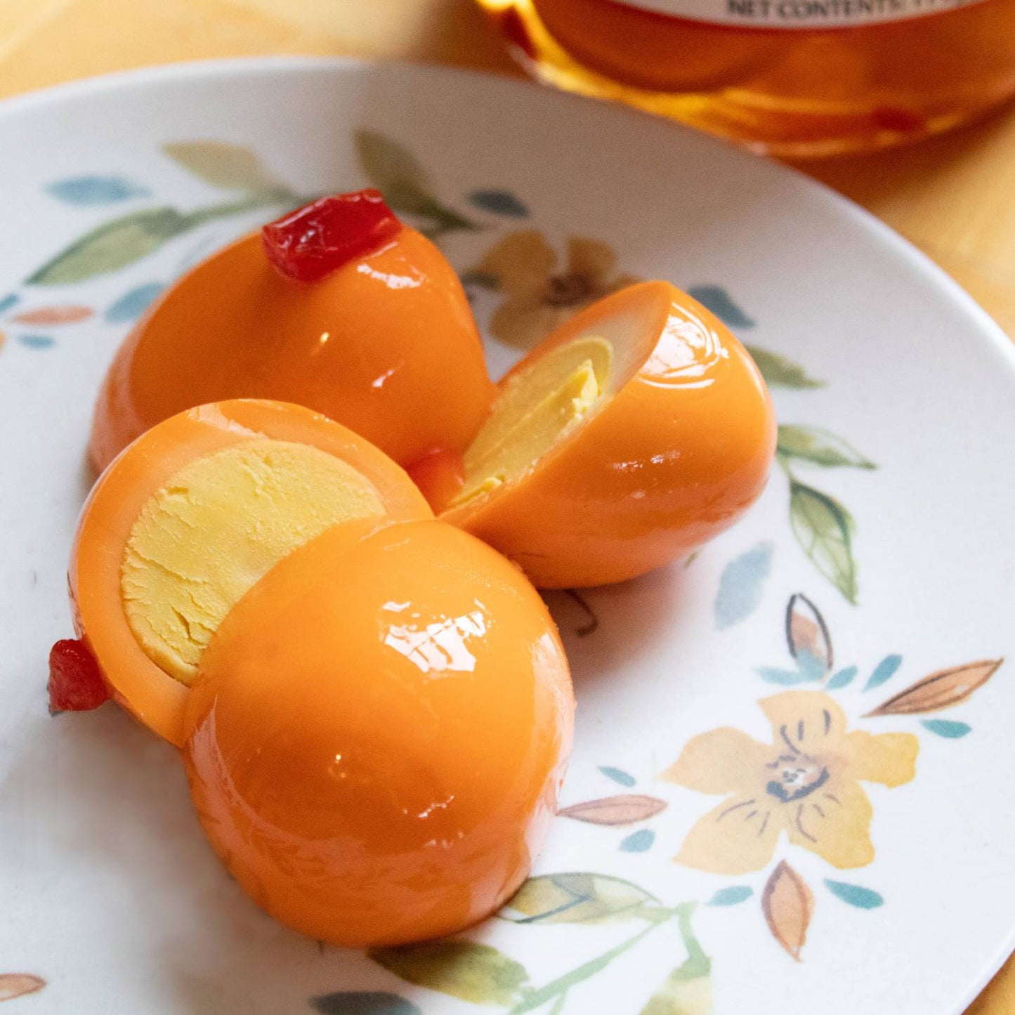 Close-up of four bright orange hot pickled eggs, one cut in half showing firm yolk, arranged on a floral patterned plate, highlighting handcrafted, locally made USA pantry favorite in Kitchen & Food collections.