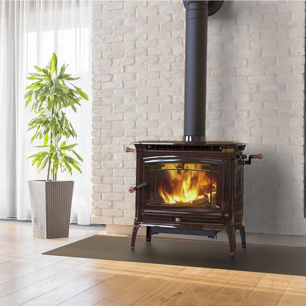 Dark metal wood heat stove with visible flames inside, standing on a protective mat against a white brick wall next to a green potted plant in a bright room, ideal for stoves and heatstoves collections.