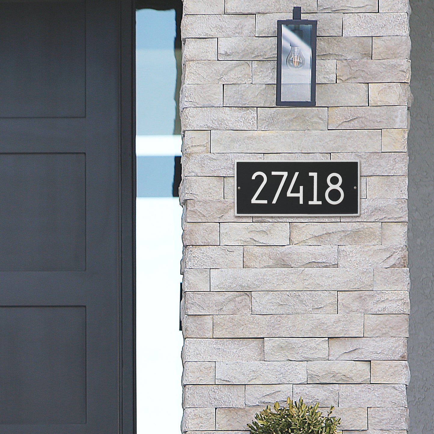 Handcrafted modern black and silver address plaque with bold white numbers mounted on a light stone exterior near a dark front door, enhancing curb appeal and value, made in USA for Home & Decor, Household Helpers, Mailboxes and Address Signs, USA Made, Best Sellers, and Promo Eligible collections.