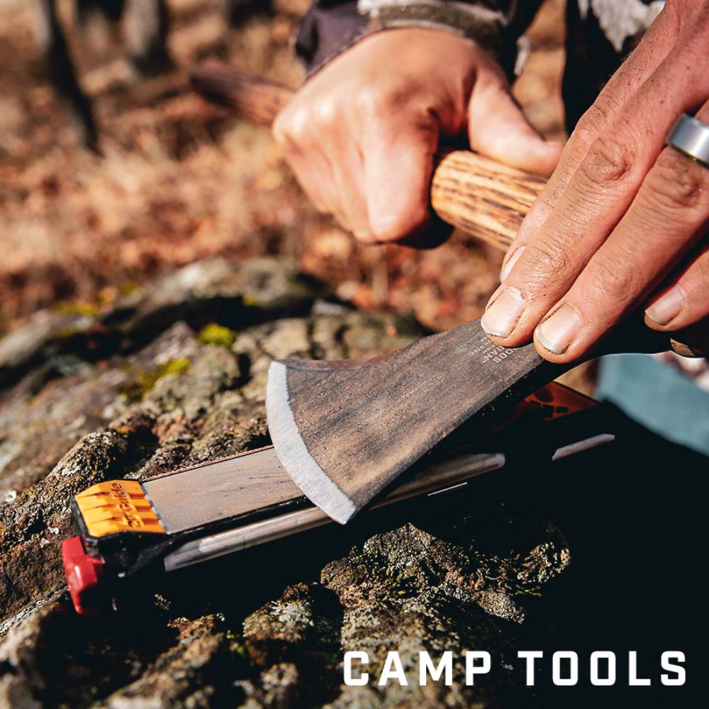 Hands using a guided sharpening tool to sharpen an axe blade outdoors on a tree stump, suitable for farm, garden, hand tools, and sharpening collections.