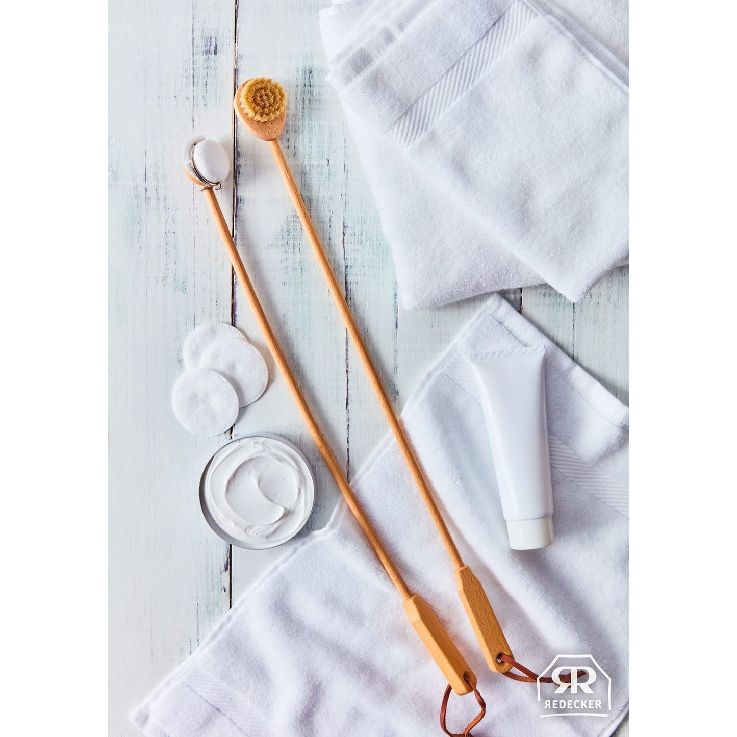 Two long-handled wooden applicators with replaceable pads and bristles alongside white towels, cotton rounds, and a cream tube, styled for Health & Wellness and Grooming collections.