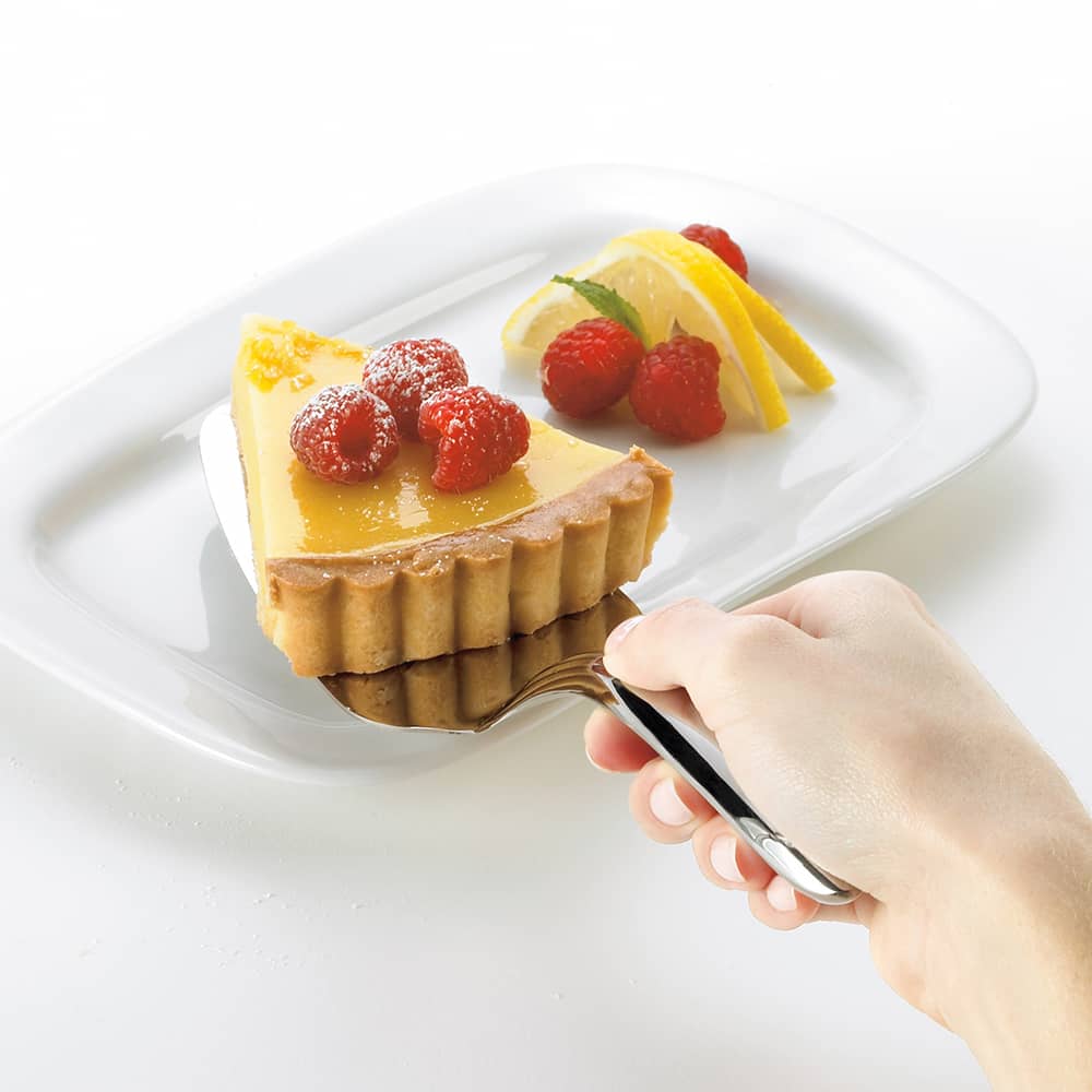 Hand holding a heavy gauge stainless steel pie server serving a slice of lemon tart garnished with raspberries and lemon slices on a white plate, perfect for Kitchen & Food and Storage and Serving collections.