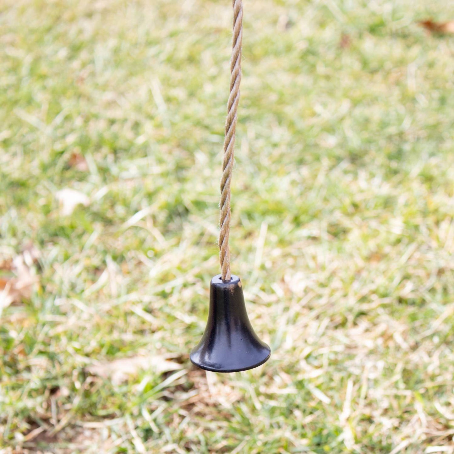 Black cast aluminum farm bell striker suspended by twisted natural rope over grass, handcrafted and Amish made, perfect for Home & Decor, Farm, Garden & Tool, and Amish Made collections.