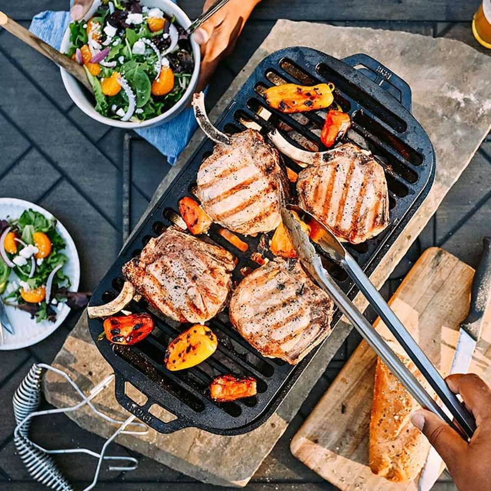 Handcrafted cast iron grill with grilled pork chops and vegetables, featuring a removable grate and slide-out ash drawer, ideal for Farm, Garden & Tool, Camping, and Cookware collections.