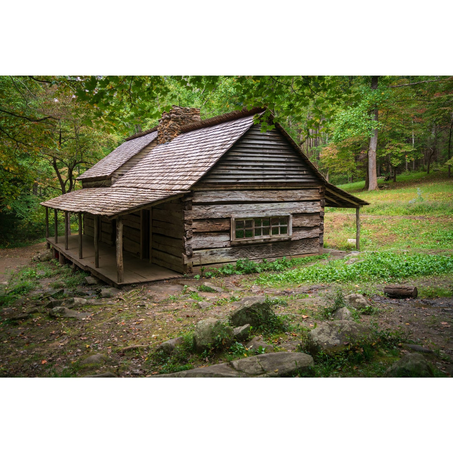 Rustic handcrafted log cabin with a wooden shingle roof and wraparound porch set in a peaceful green forest, evoking heritage and traditional lifestyle themes.