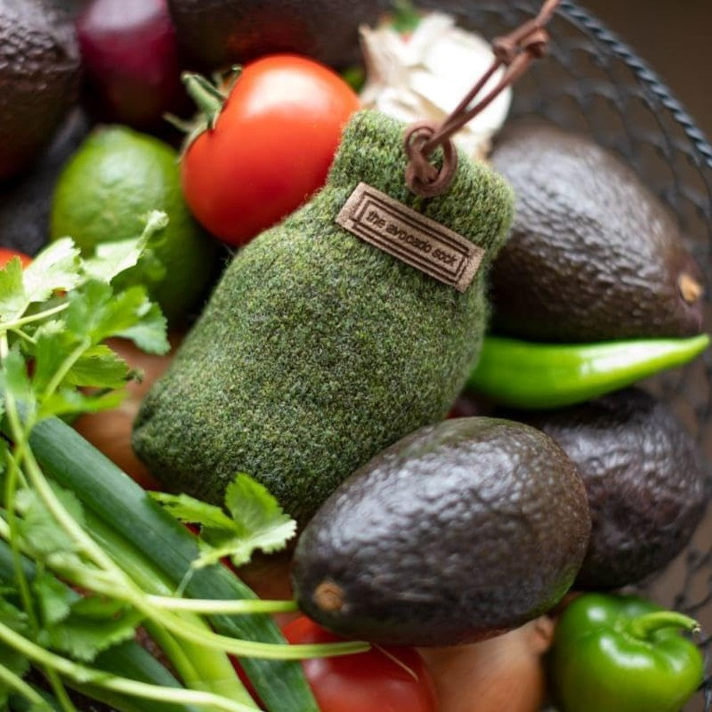 Olive green natural wool ripening sock with leather loop and label, sized to hold one avocado, surrounded by fresh produce, featured in Kitchen & Food and Best Sellers collections.
