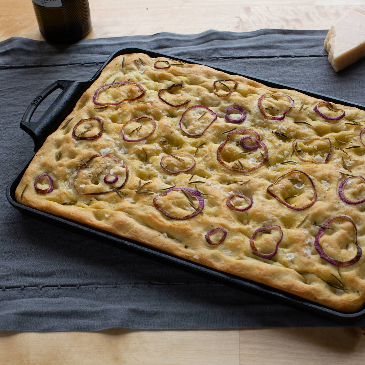 Handcrafted cast iron baking pan with two handles, holding freshly baked focaccia topped with red onion slices and herbs, featured in Kitchen & Food, Cookware, Cast Iron, Baking Supplies, USA Made, Best Sellers, and Promo Eligible collections.