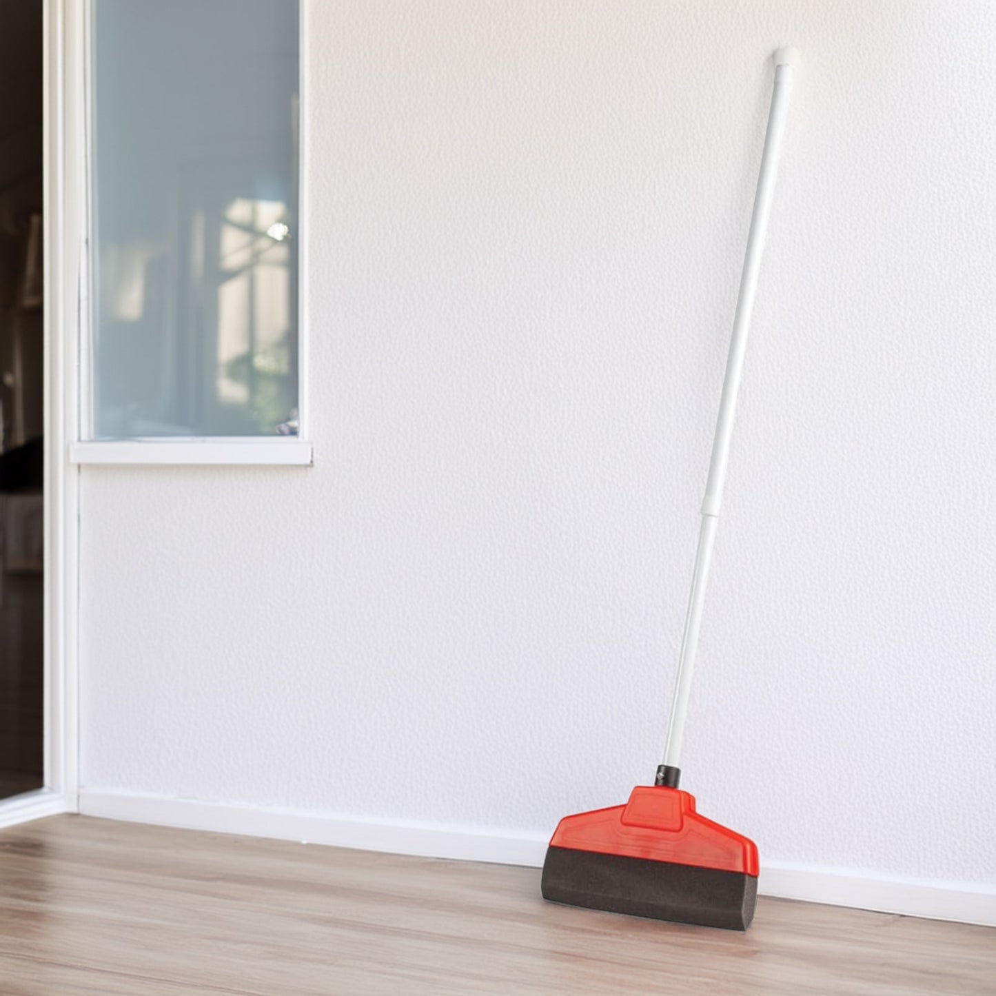 Handcrafted electrostatic broom with a polyurethane foam brush and red plastic housing leaning against a white wall on a wood floor, ideal for Home & Decor and Household Cleaning collections.