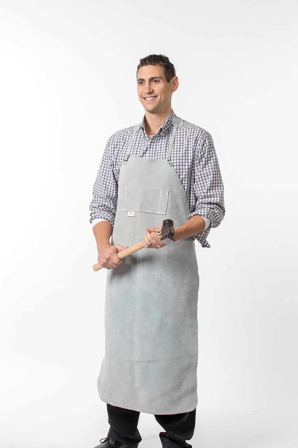 Man wearing a heavyweight handmade leather apron holding a hammer, shown in a clean studio setting, suitable for farm, garden, woodworking, and hardware tasks.