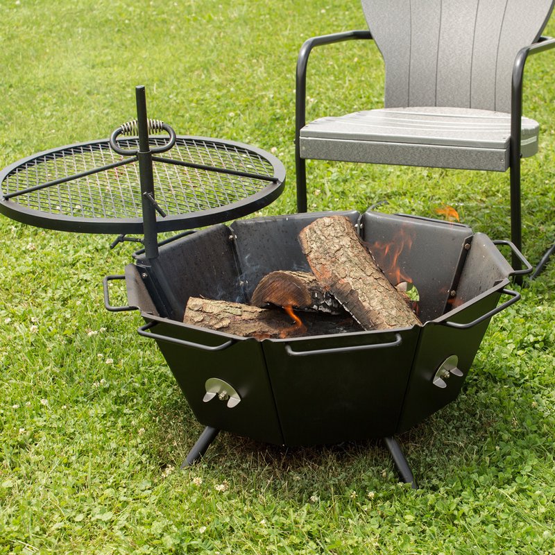 Heavy-duty steel backyard fire pit grill with a detachable round cooking grate beside it, burning wood inside, placed on grass next to an outdoor chair, ideal for Farm, Garden & Tool, Stoves, Camping, and USA Made collections.