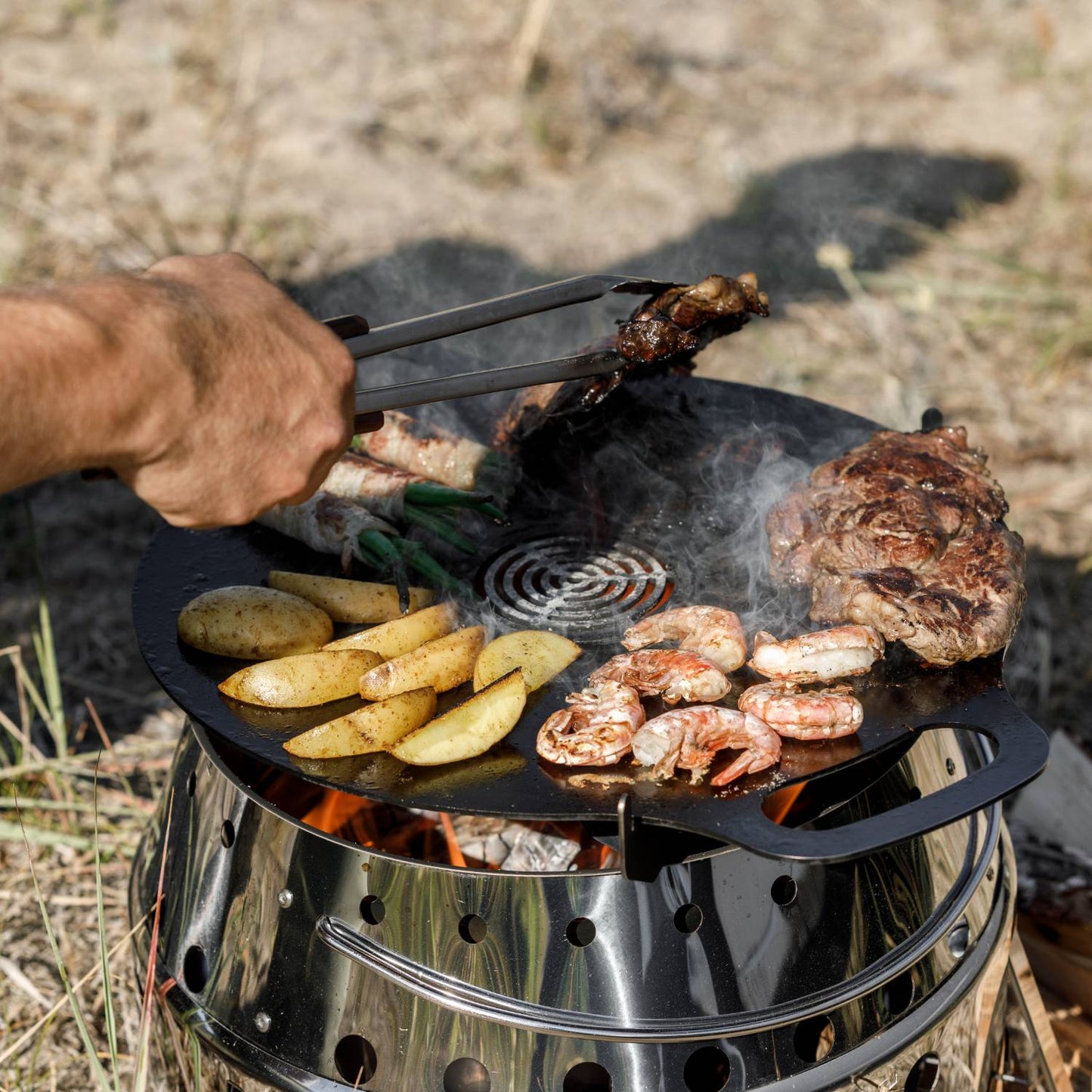 Round metal insert with concentric circular design placed in the center of a griddle plate grilling shrimp, steak, potatoes, and green beans, ideal for Farm, Garden & Tool, Camping, Grilling, and Stoves collections.