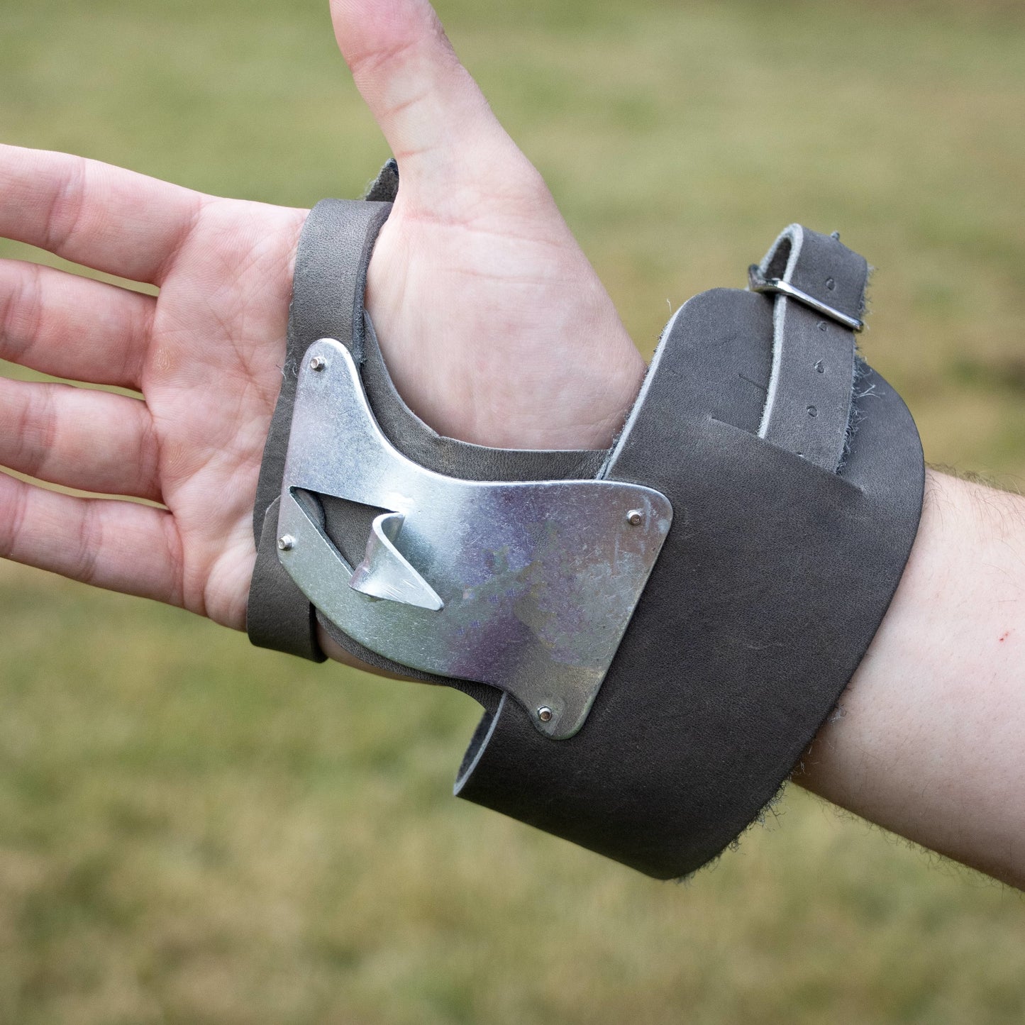 Hand wearing a brown leather palm pad with adjustable double wrist strap and galvanized steel single hook for husking corn, part of Farm, Garden & Tool, USA Made, Best Sellers collections.