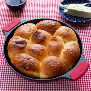 Handcrafted cast iron baker's skillet with red silicone grip handles, naturally seasoned for even heat, showcasing freshly baked golden dinner rolls, part of Kitchen & Food, Cookware, Cast Iron, USA Made, Best Sellers, and Promo Eligible collections.