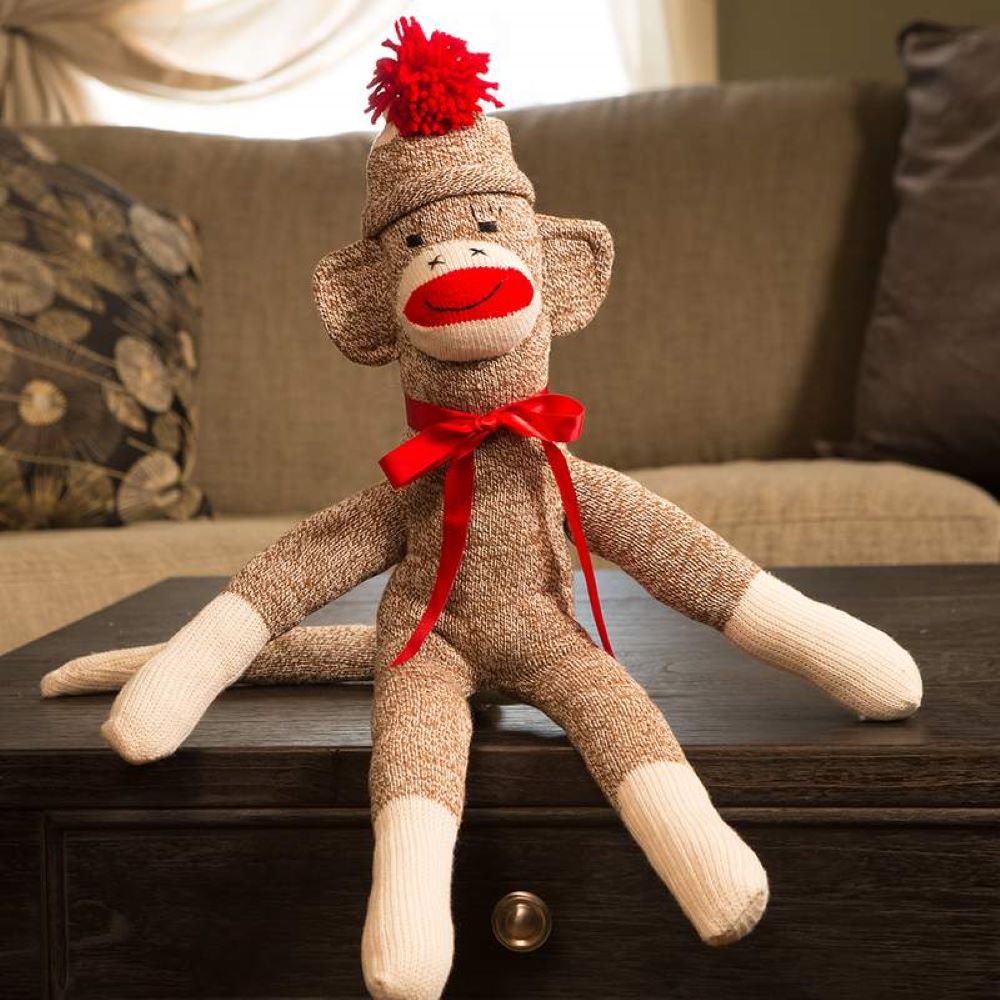 Handcrafted sock monkey made in the USA from classic red-heeled socks, featuring a red pom-pom hat, bright red bow, and fiberfill stuffing, perfect for indoor play and children's toys collections.
