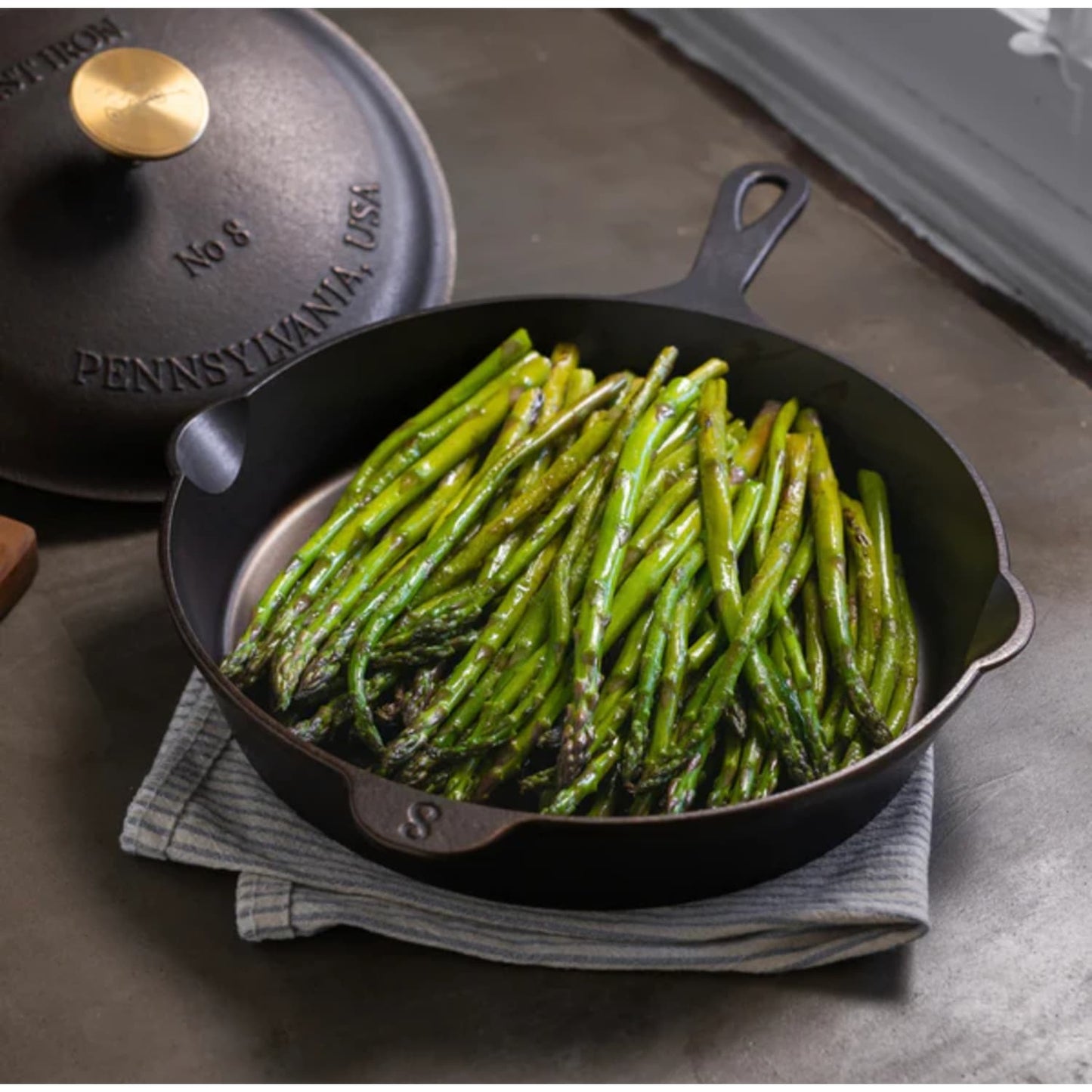 Handcrafted lightweight cast iron skillet with sautéed asparagus, featuring a smooth surface and fitted lid embossed with Pennsylvania USA, ideal for Kitchen & Food, Camping, and Cast Iron collections.