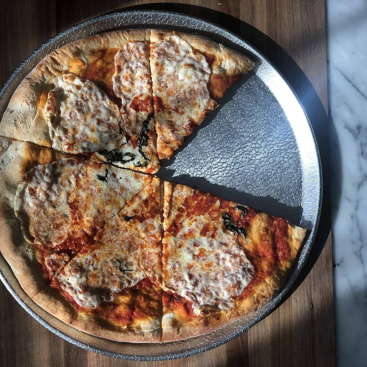 15-inch aluminum pizza pan with a textured pebble surface for improved airflow, shown holding a cheese pizza with one slice removed, ideal for kitchen, cookware, and best seller collections.