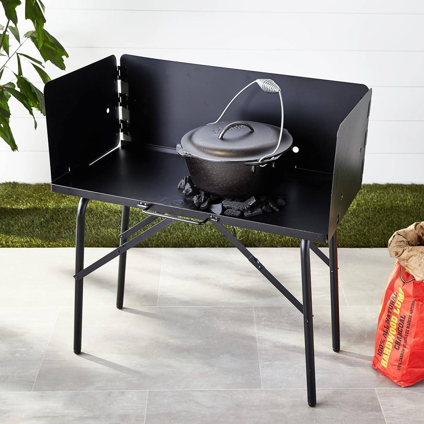 Black all-steel collapsible outdoor cooking table with three-sided windscreen holding a cast iron pot over hot coals, ideal for Farm, Garden & Tool, Camping, Best Sellers, and Promo Eligible collections.