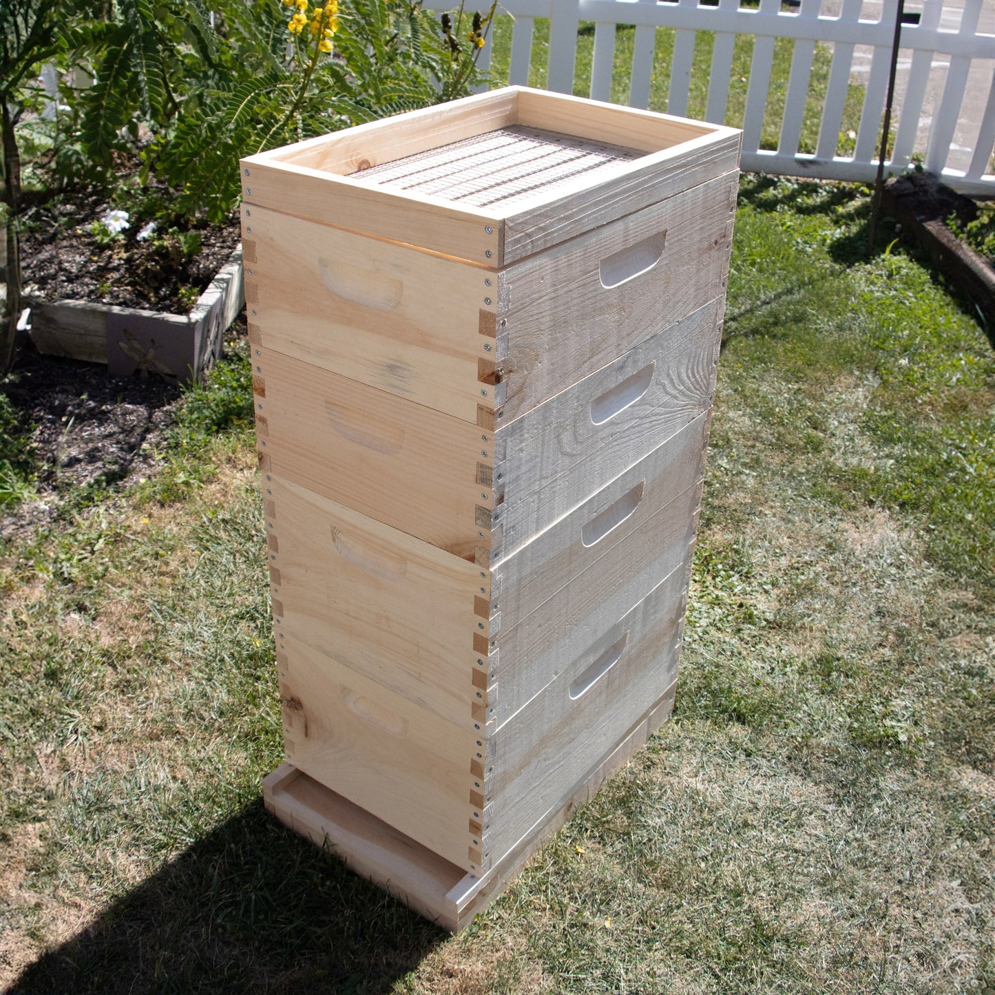 Stacked wooden 8-frame beehive boxes with a handcrafted candy board feeder on top, made in the USA, displayed outdoors in a garden setting, featured in Farm, Garden & Tool and Beekeeping Supplies collections.