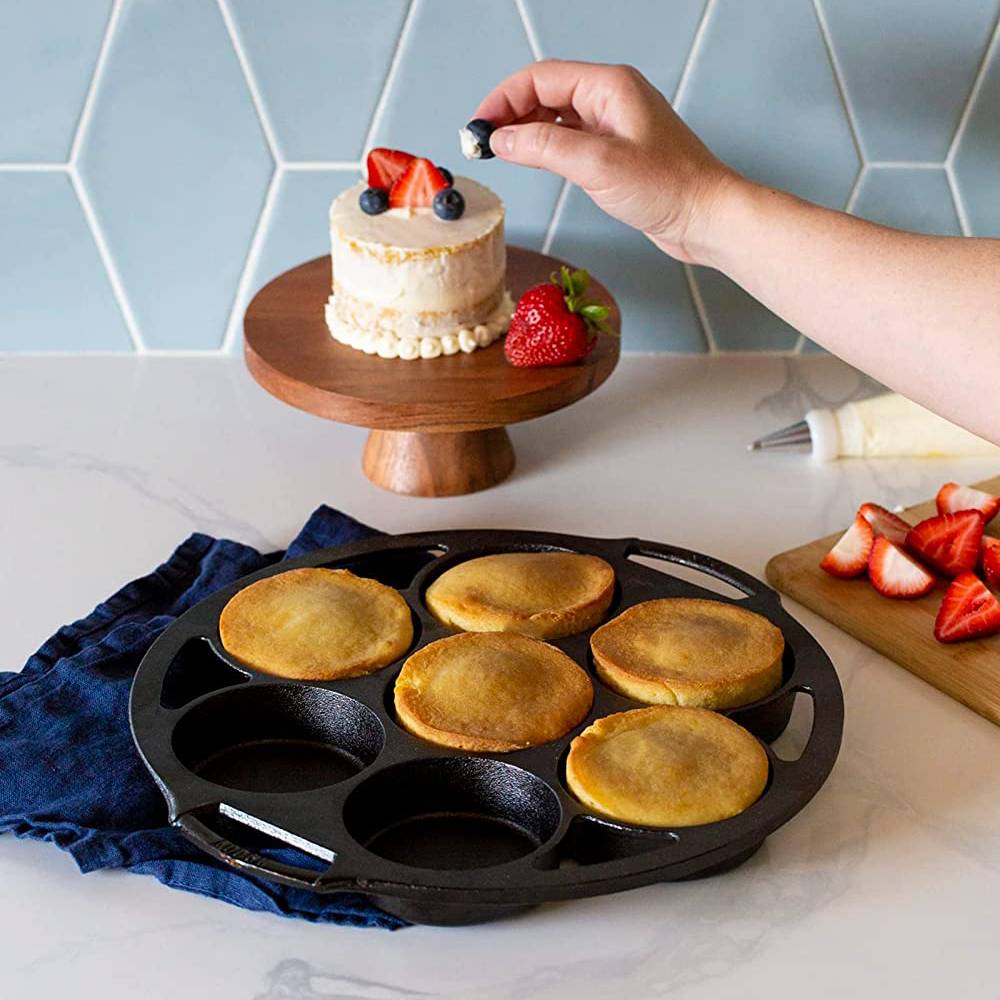 Handcrafted cast iron mini cake pan with six golden cakes, a small decorated cake on a wooden stand, fresh strawberries, and blueberries, featured in Kitchen & Food, Cast Iron, and USA Made collections.