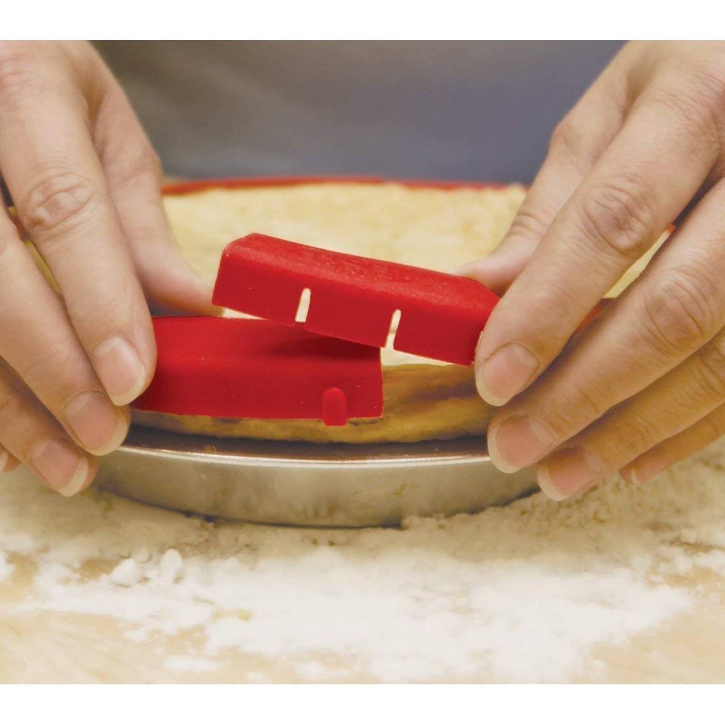 Hands placing a red silicone shield around a pie crust in a metal pie pan on a floured surface, designed to protect the crust while baking, featured in Kitchen & Food and Baking Supplies collections.