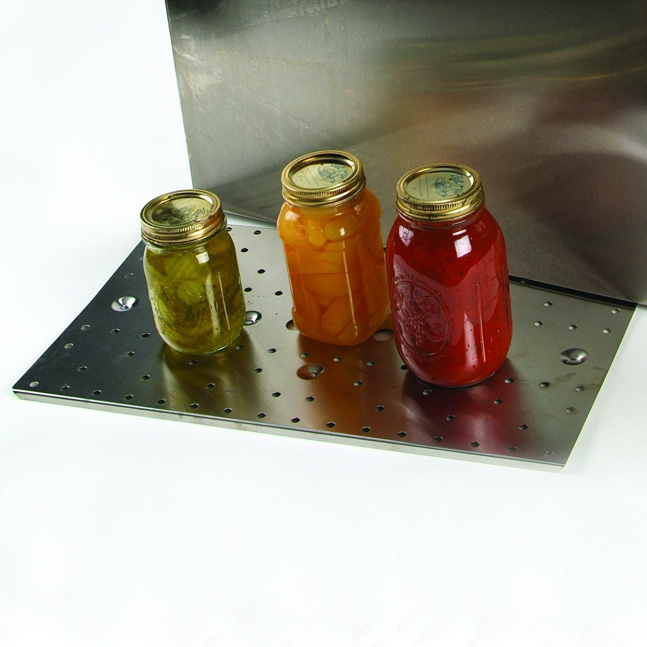 Sturdy replacement canning shelf with perforated metal surface holding three sealed glass jars, designed for stable jar support and even heating in Amish-made stovetop water bath canners, ideal for food preservation and kitchen use.