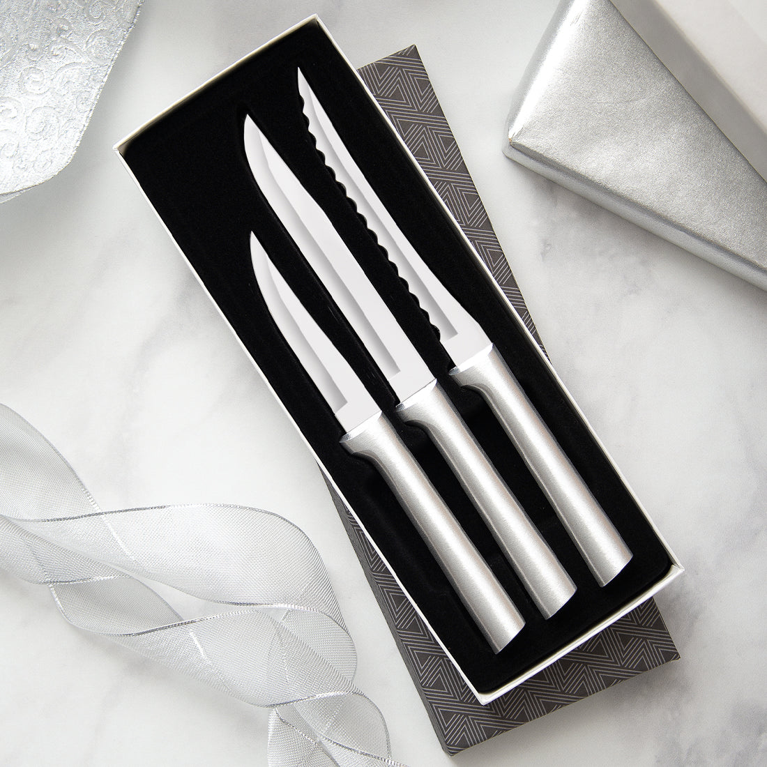 Set of three handcrafted stainless steel knives with smooth silver handles, including serrated tomato slicer, utility/steak knife, and heavy-duty paring knife, made in USA for kitchen and food prep.
