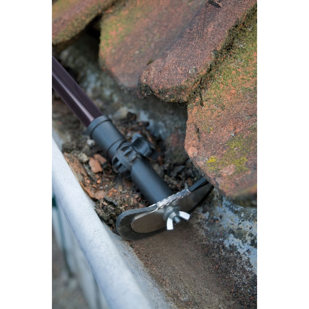 Close-up of a durable stainless steel gutter cleaner with rubber lip and adjustable telescoping handle removing debris from roof gutters, ideal for Farm, Garden & Tool and Lawncare collections.