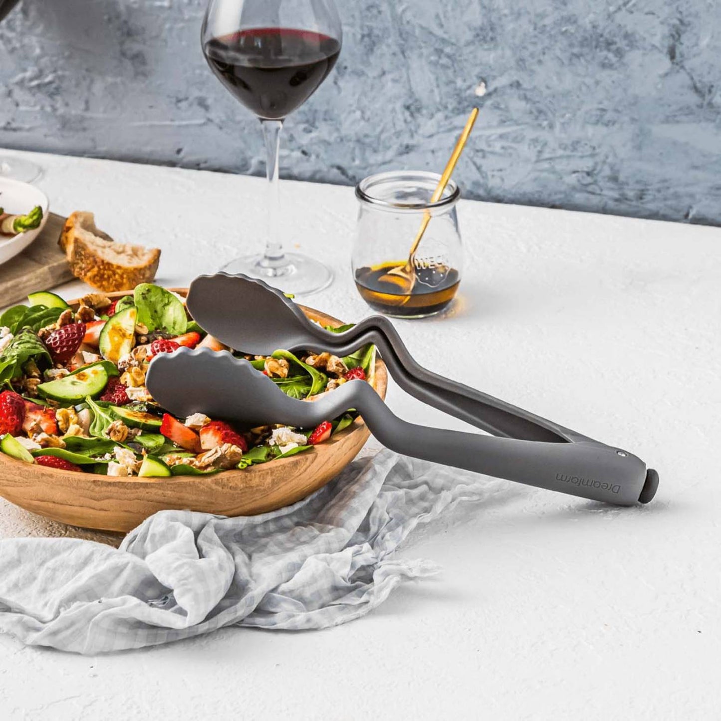 Gray nylon cooking tongs with an ergonomic bend to keep tips elevated and mess-free, resting beside a fresh vegetable and berry salad, suitable for Kitchen & Food, Kitchen Gadgets, Cooking and Baking Helpers, Best Sellers, and Promo Eligible collections.