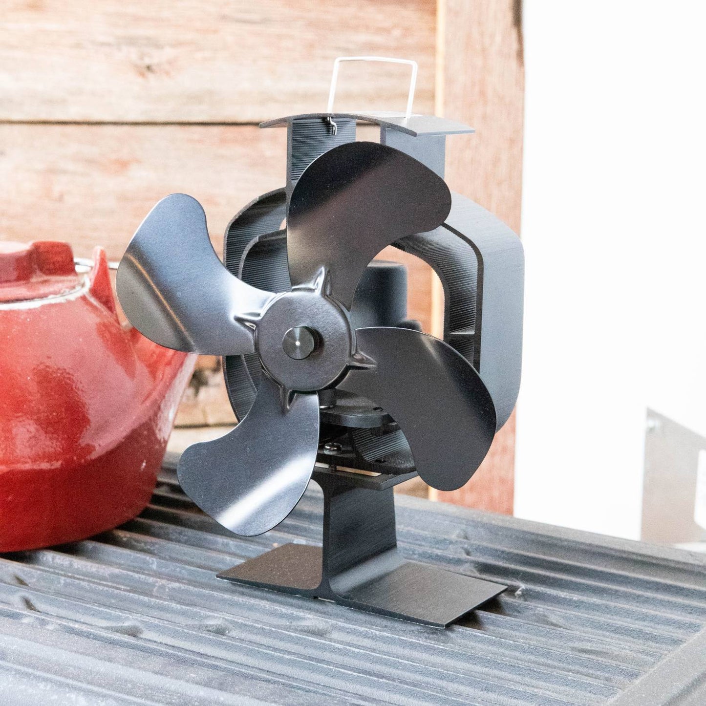 Handcrafted black metal heat-powered oscillating stove fan with four curved blades and sturdy base, designed to circulate warm air efficiently in stoves and hearth accessories collections.