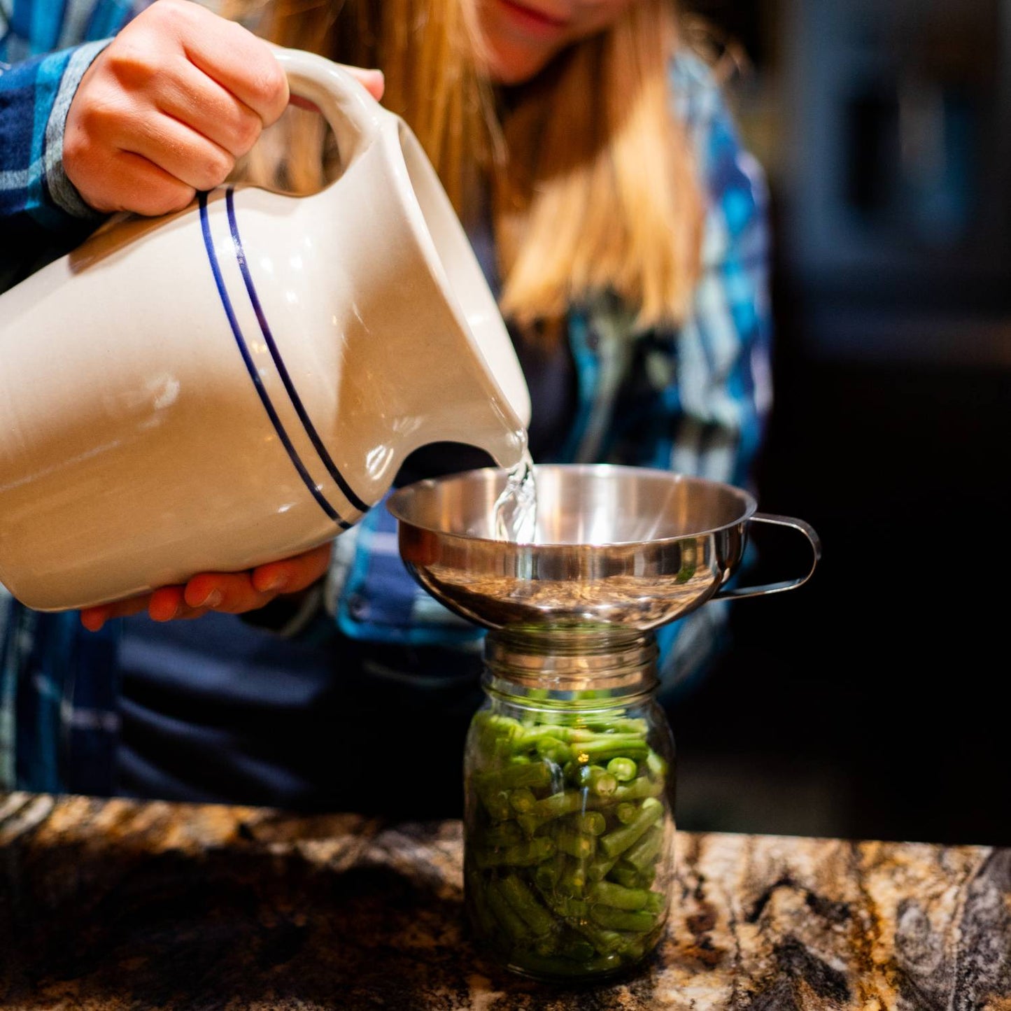 Person pouring water from a ceramic pitcher into a stainless steel funnel placed on a jar filled with green beans, showcasing a neat food preservation setup in Kitchen & Food and Canning Accessories collections.
