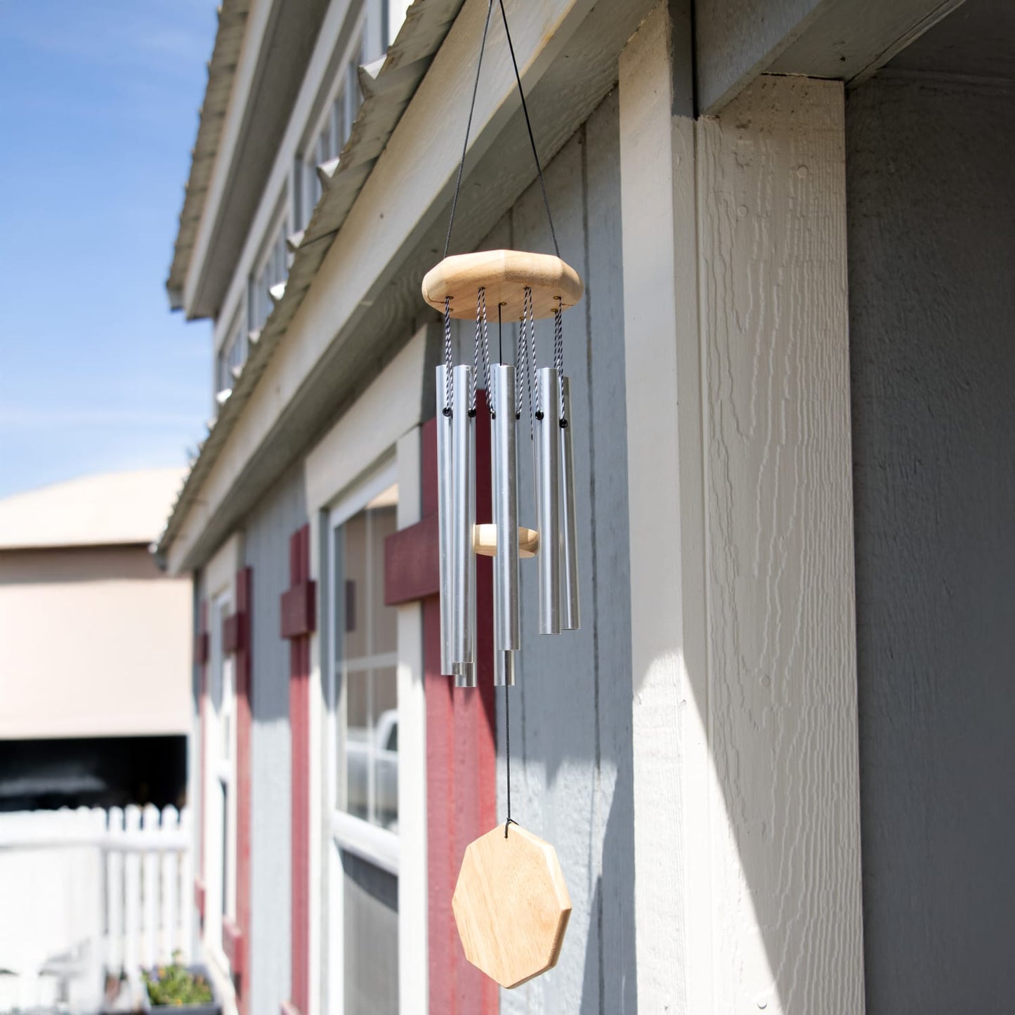 Handcrafted windchime with polished metal tubes and an octagon wooden windcatcher hanging from a porch, ideal for adding peaceful sound to outdoor spaces in Farm, Garden & Tool and Garden Accessories collections.