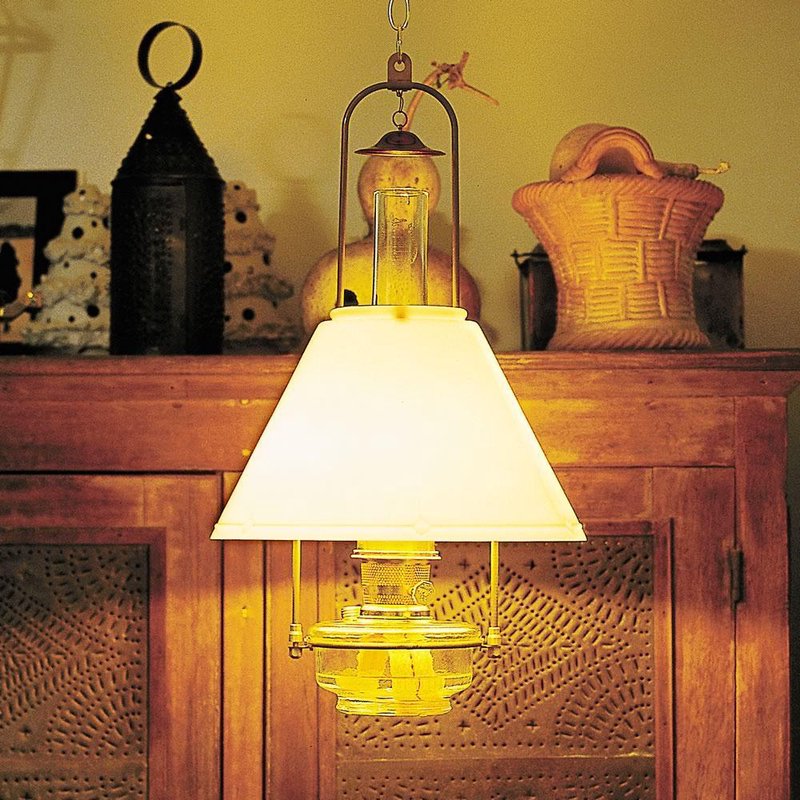 Warm glowing hanging lamp with a clear glass oil reservoir and brass tilt-frame hanger, illuminating rustic wooden furniture, featured in Farm, Garden & Tool and Lamps & Lighting collections.