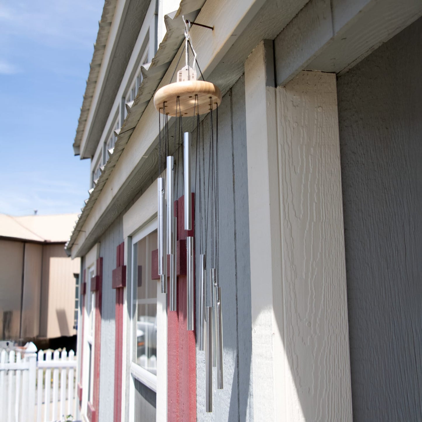 Handcrafted 21" spiral wind chime with silver metal tubes and a wooden top, hanging outdoors on a gray and red building, perfect for garden accessories and farm use.