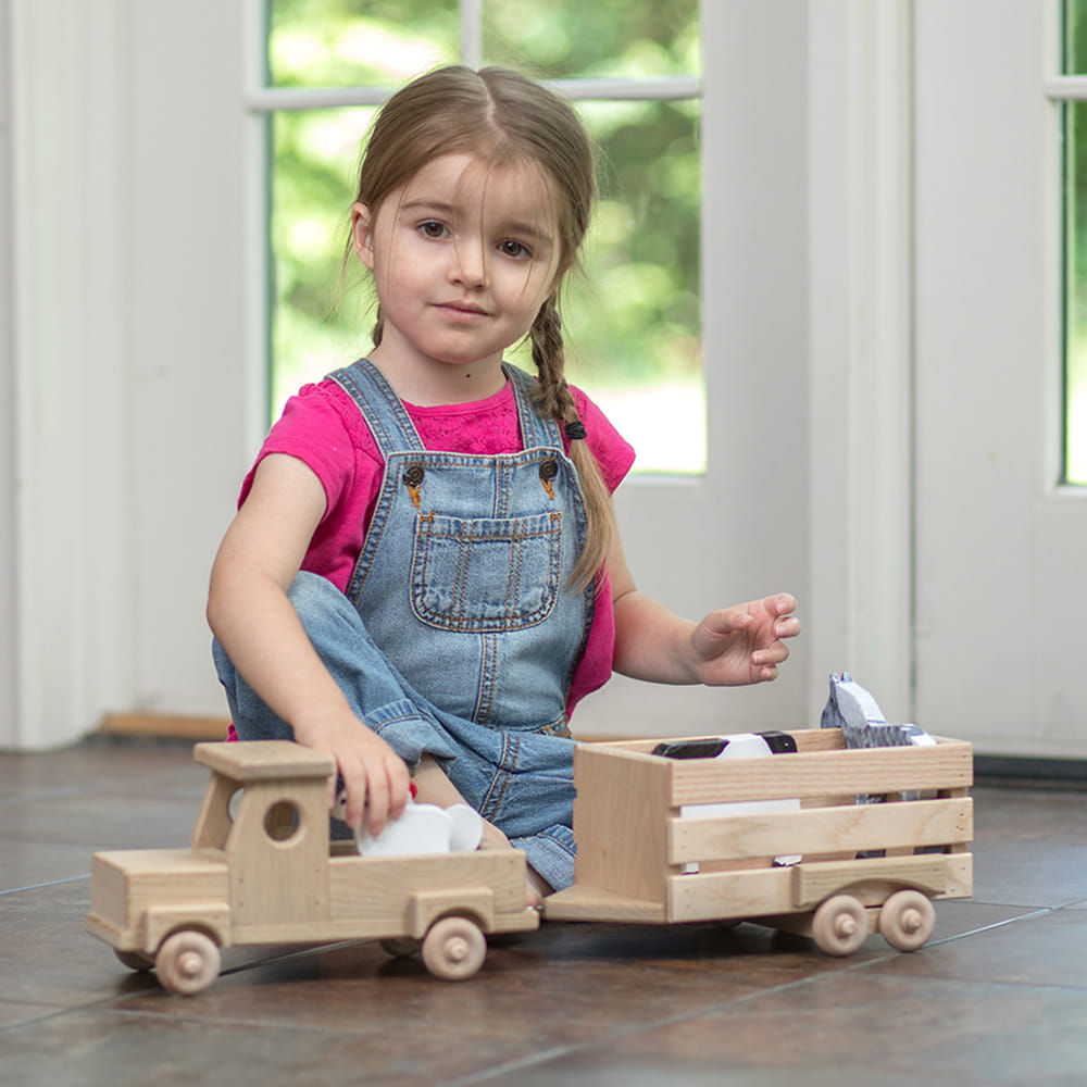 Young girl playing indoors with a handcrafted wooden truck and stock trailer made in USA, Amish made, ideal for children's toys, indoor play, and wooden toys collections.