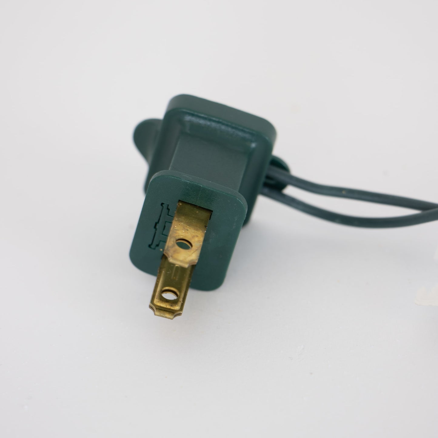 Close-up of a green two-prong electrical plug with attached cord, suitable for indoor use and compatible with lighted holiday decorations in Home & Decor and Promo Eligible collections.