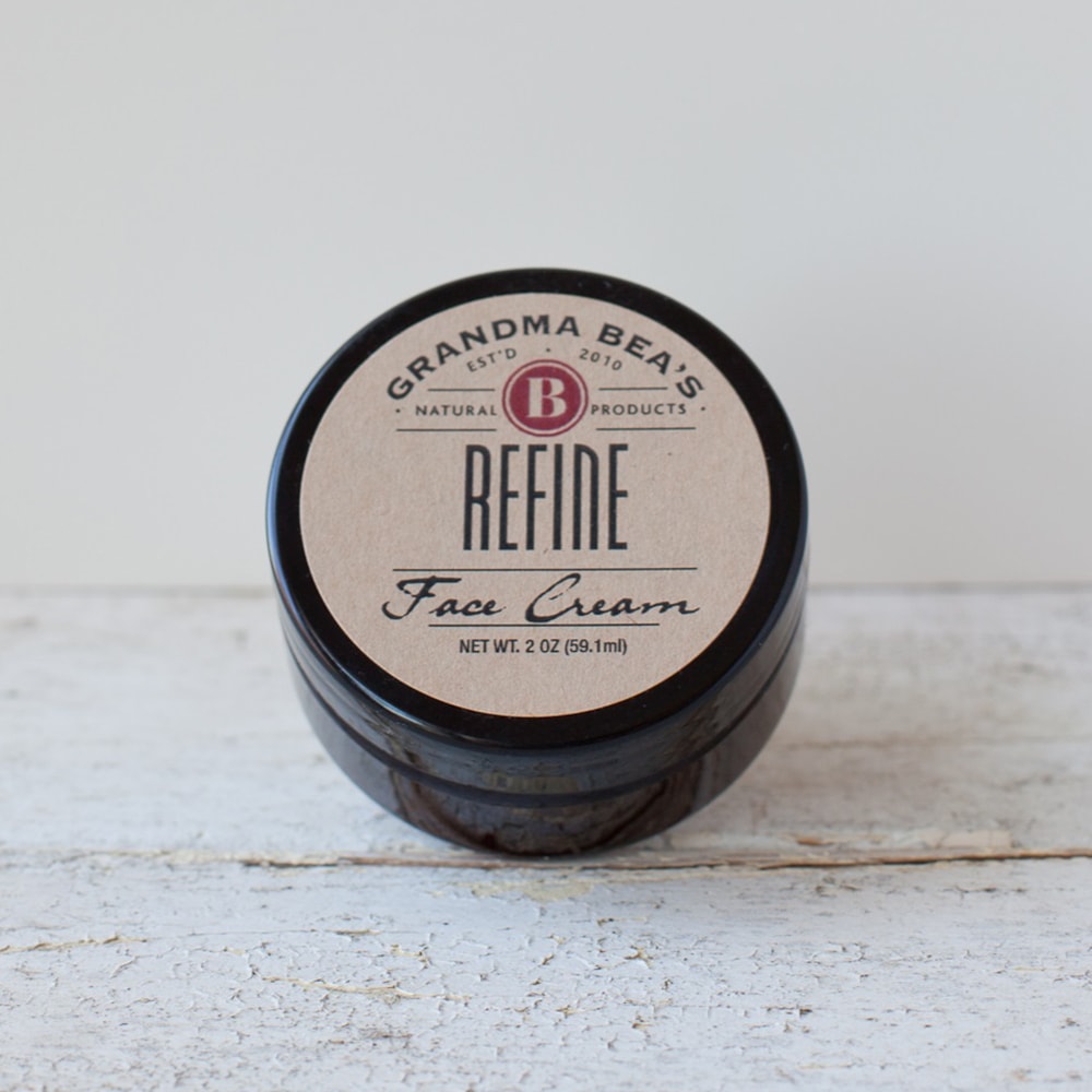 Small amber glass jar of handcrafted all-natural face cream with a simple kraft paper label, featured in Health & Wellness and USA Made collections.