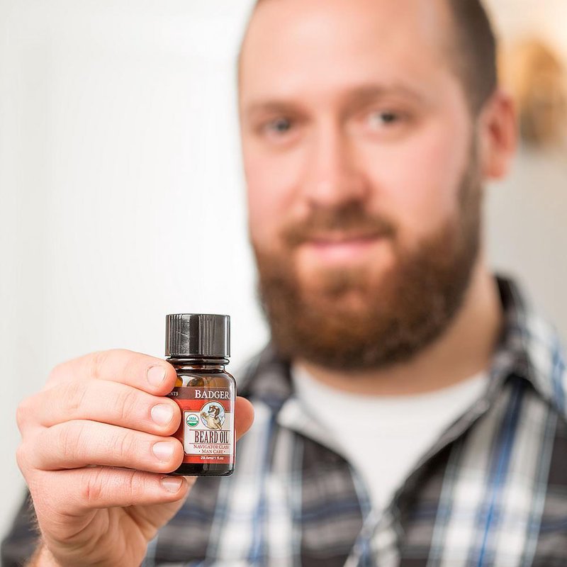 Man holding a small amber glass bottle of handcrafted beard oil made in USA, featured in Health & Wellness, Grooming, USA Made, and Best Sellers collections.