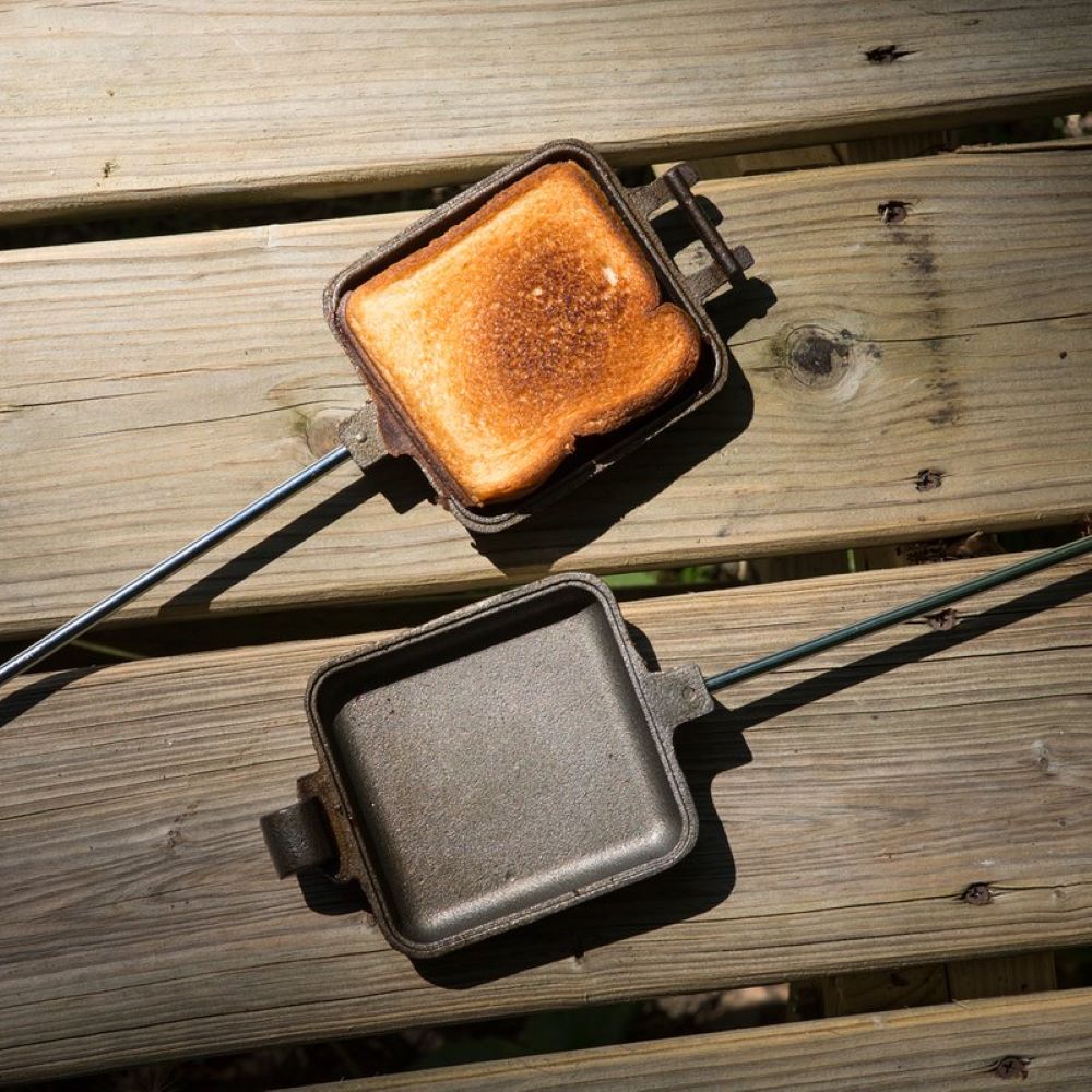 Open cast iron square pie iron with long metal handle and wooden grip, showing toasted bread inside, ideal for camping and featured in Farm, Garden & Tool, Best Sellers, and Promo Eligible collections.