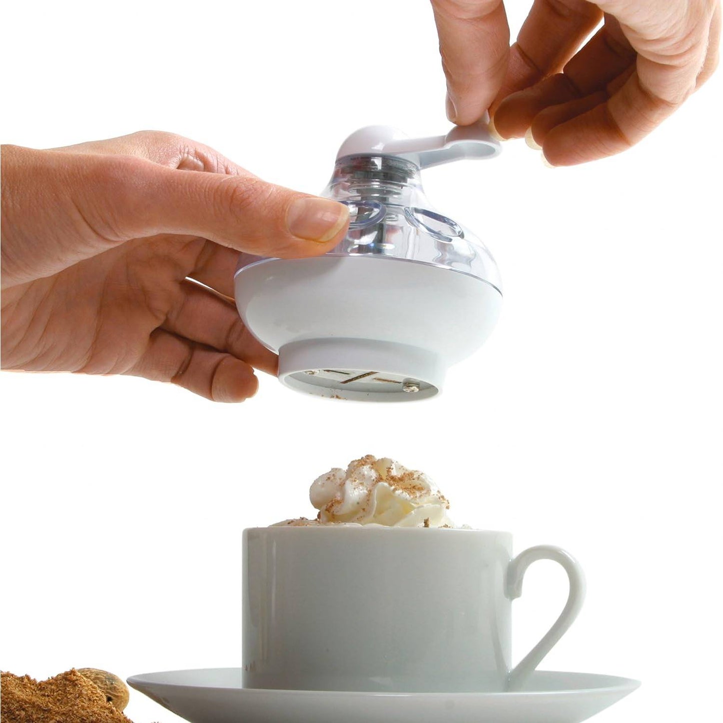 Handheld nut and spice grinder with a clear body and white crank handle, grinding fresh spices over a cup topped with whipped cream, ideal for Kitchen & Food and Brewing Coffee and Tea collections.